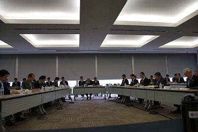 コの字型に並べられた机に、大勢の男性が座って会議をしている様子